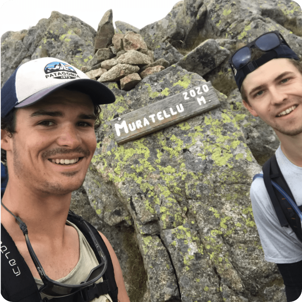 Two men in front of a sign afixed to a rock reading Muratellu 2020 M